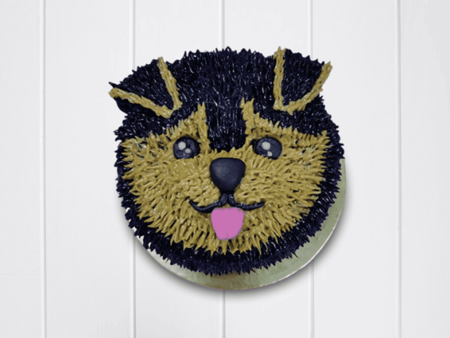 Cute dog face cake with expressive eyes, floppy ears, and tongue out in brown and black icing.